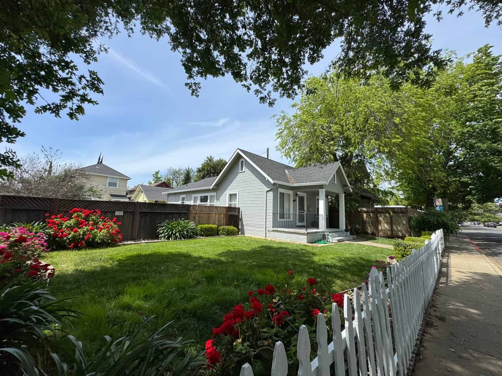 Charming white house with a lush green front yard and colorful flowers, under a bright blue sky.