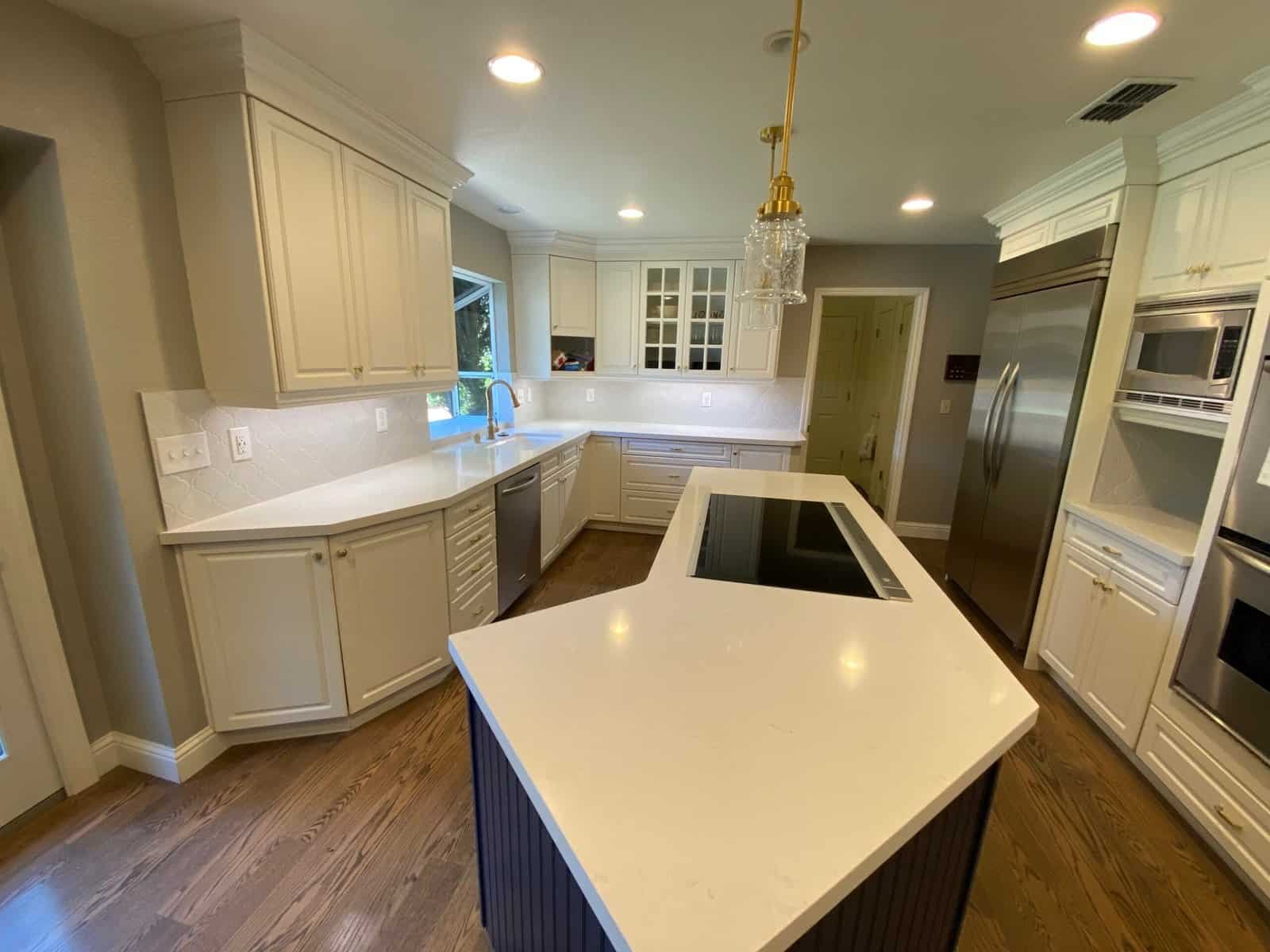 Bright kitchen with white cabinets, island, and stainless steel refrigerator and oven.