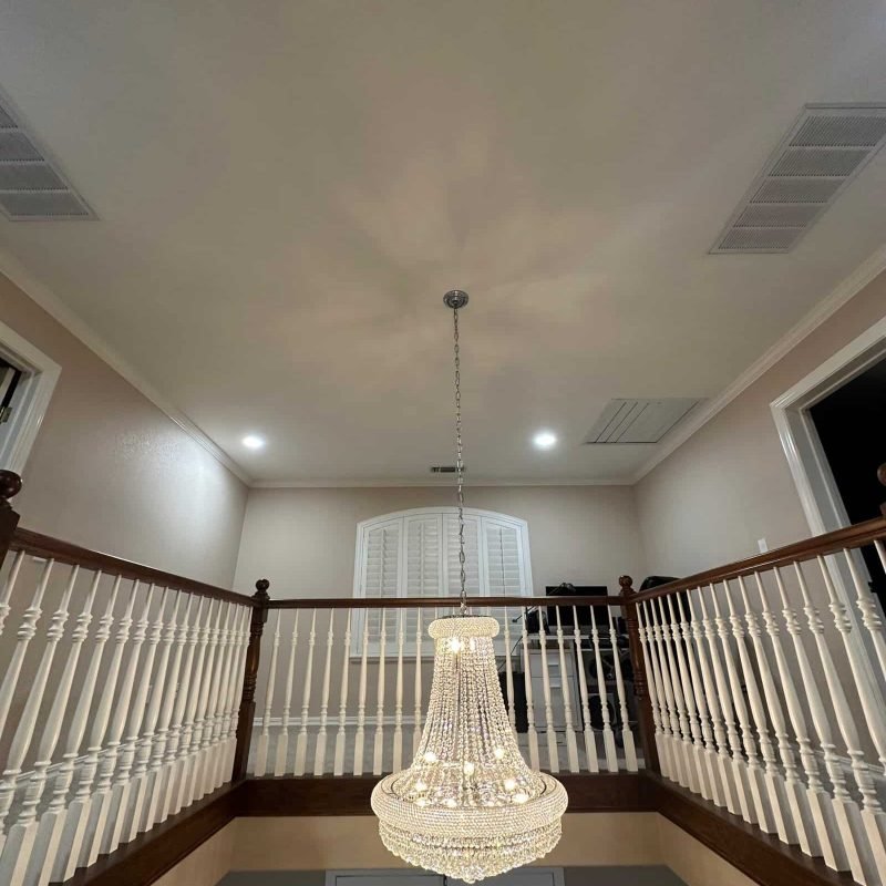 Chandelier lighting fixture hanging in a spacious home interior with high ceilings.