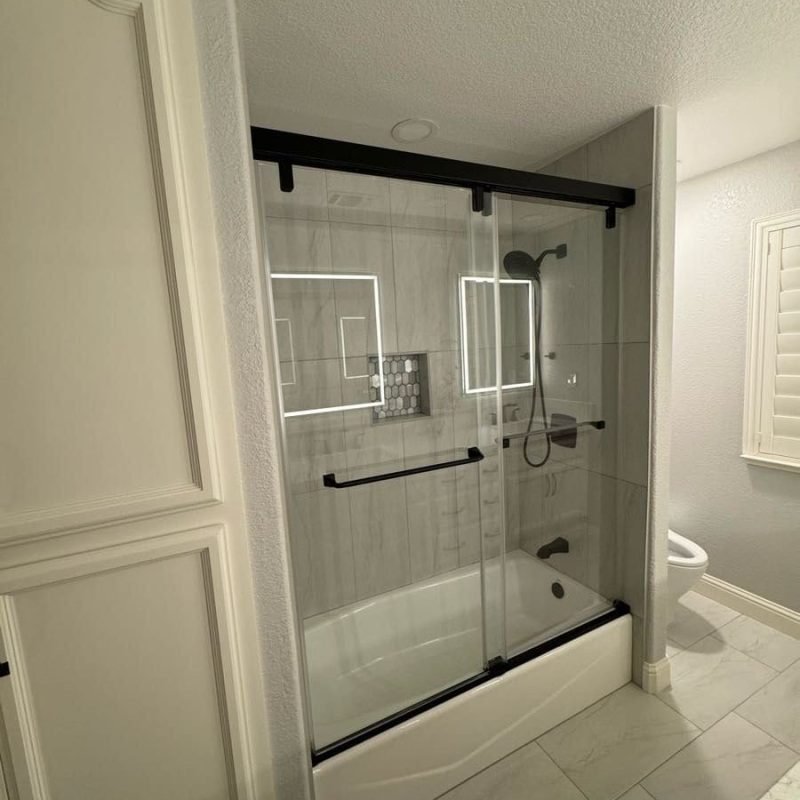 Glass shower with black frame and sliding doors in a modern bathroom.