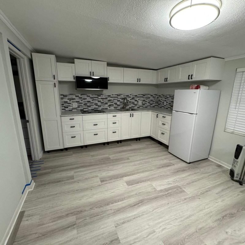 Bright modern kitchen with white cabinets, gray backsplash, and appliances.