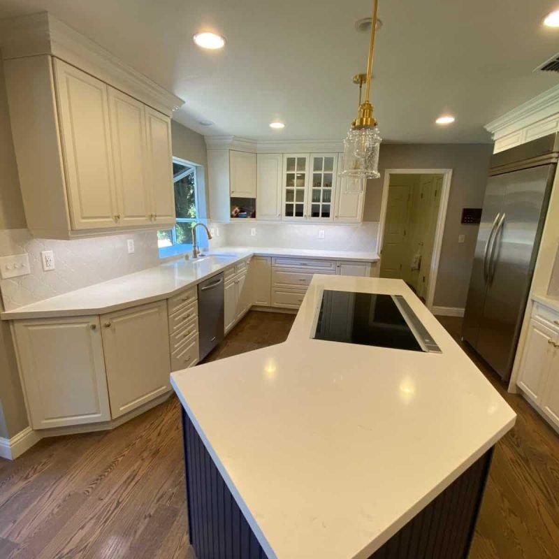 Bright kitchen with white cabinets, island, and stainless steel refrigerator and oven.