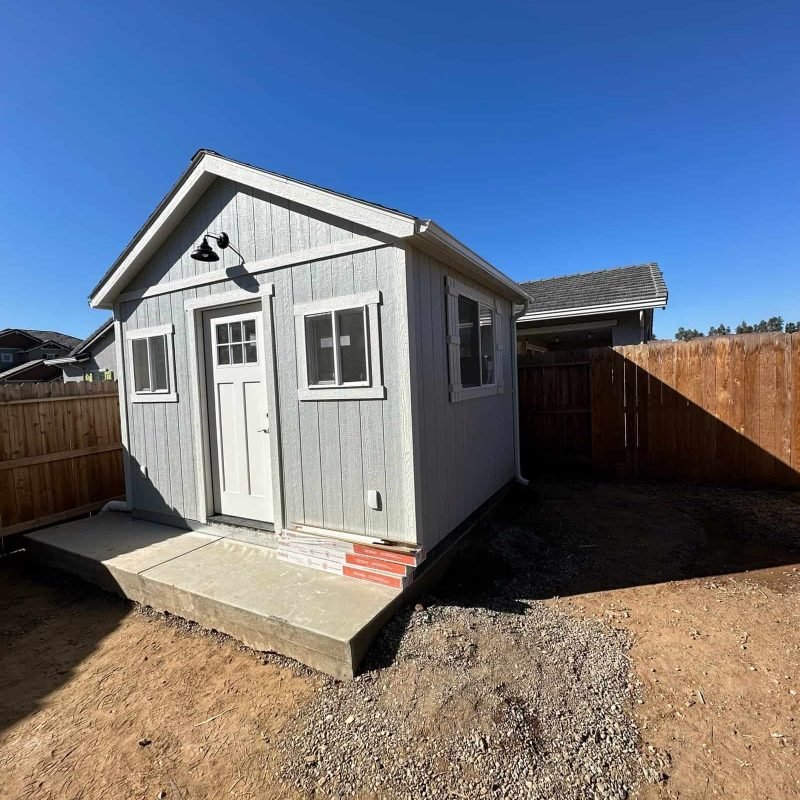 Small backyard shed with white siding, windows, and a concrete foundation.